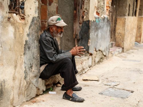 Free Elderly man in a leather jacket sitting on a weathered street, capturing urban decay and solitude. Stock Photo