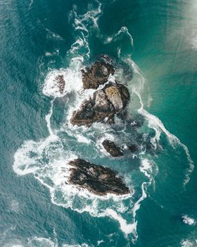 Stunning aerial view of ocean rocks and waves in Tofino, BC, showcasing nature's raw beauty.