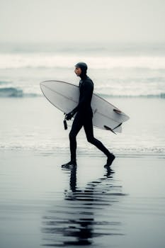 Surfer in a wetsuit walks with surfboard on Tofino's beach, BC, Canada.