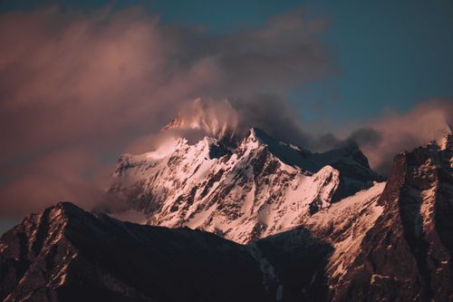 Free A dramatic snow-covered mountain peak basking in warm sunset hues, enveloped by mist and clouds. Stock Photo