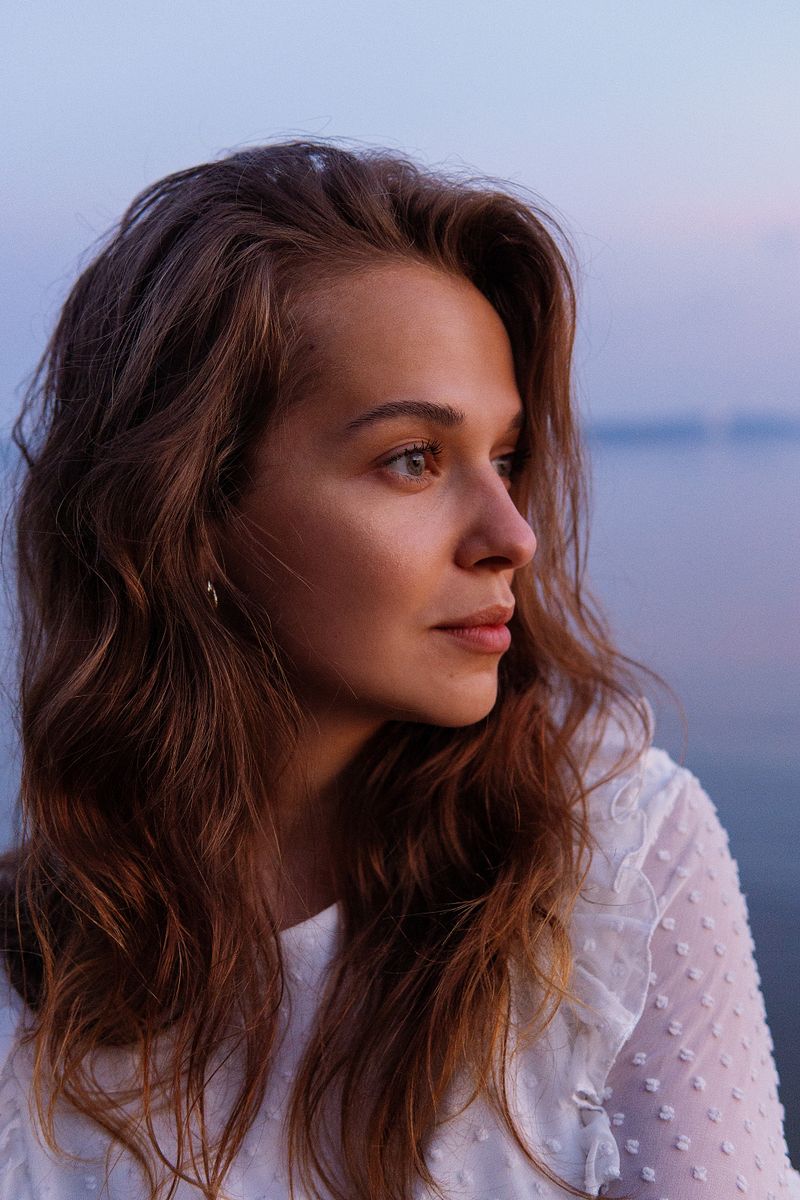 Woman with wavy hair gazing at the sea at dusk