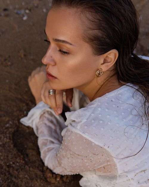 Free Close-up portrait of a woman lying on sand with wet hair, wearing a white dress and gold earrings. Stock Photo