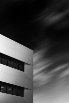 Striking black and white image of modern building capturing geometric design and motion-blurred sky.