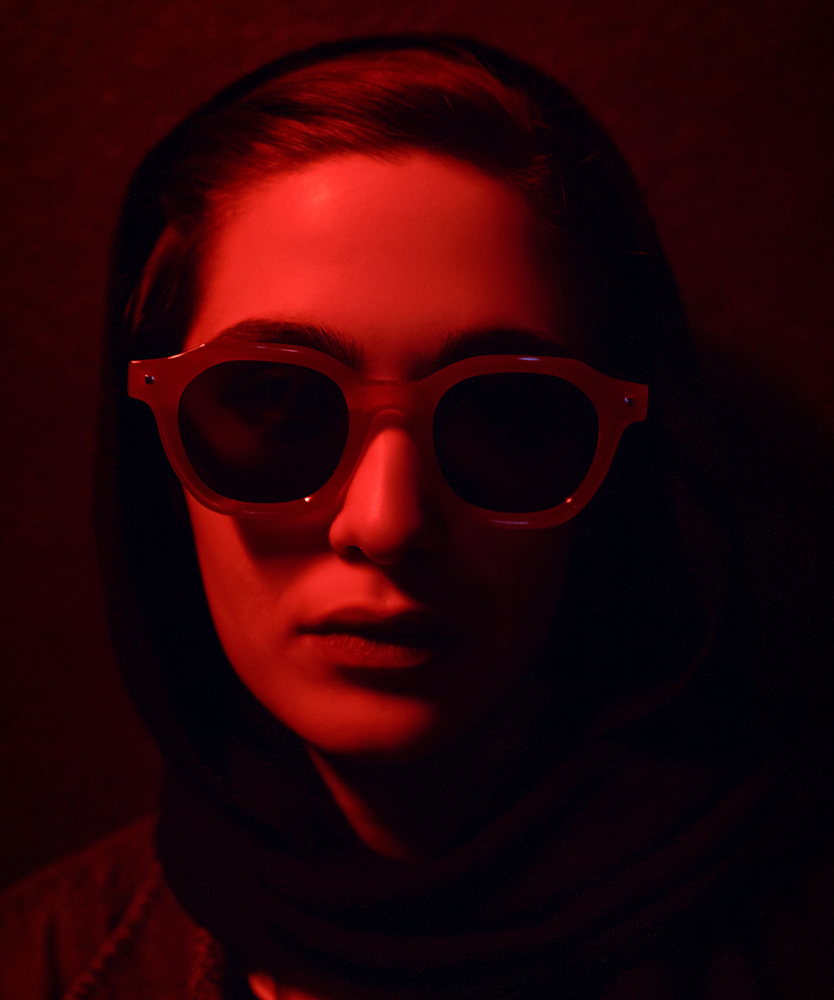 A mysterious woman wearing sunglasses under red lighting creates a moody atmosphere.