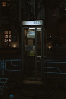 Dark urban street with an illuminated vintage telephone booth at night.