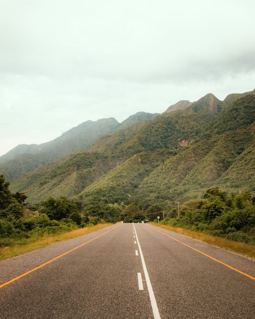 Free A tranquil road cutting through lush green mountains under a cloudy sky, epitomizing nature's serene beauty. Stock Photo