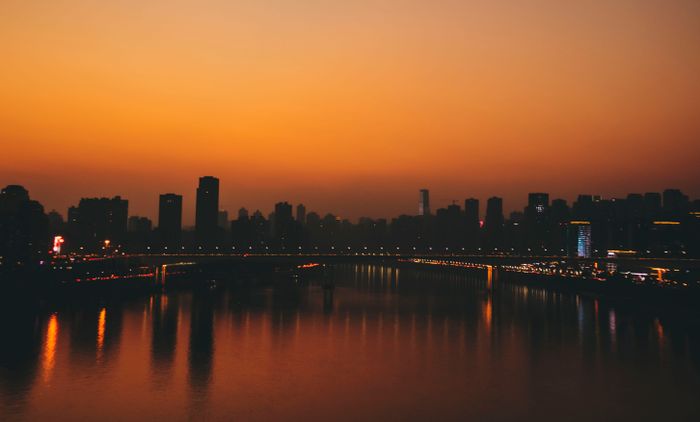 City skyline silhouetted at dusk across a river — photo by Tinny HU on Pexels