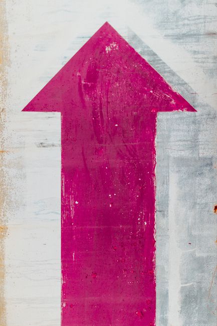 Close-up of a painted pink arrow on a worn-out textured wall in Málaga.