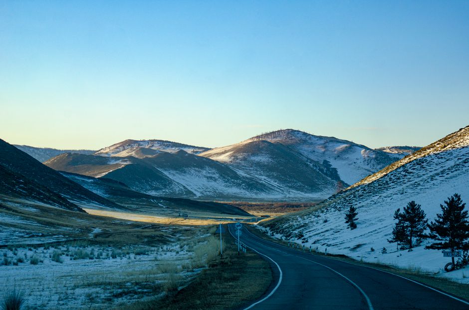 A picturesque road winding through snow-capped mountains at sunrise with a clear sky.