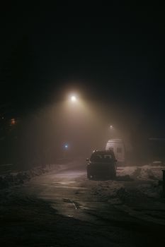 Moody night street scene with cars parked under glowing streetlights.