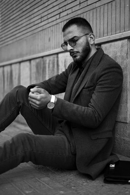 Monochrome close-up of a man in a suit jacket, sitting against an urban wall.
