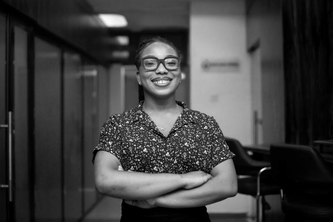 Smiling woman in eyeglasses stands confidently in an office corridor