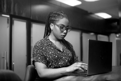Free African American woman focused while working on a laptop in an office, showcasing a professional setting. Stock Photo