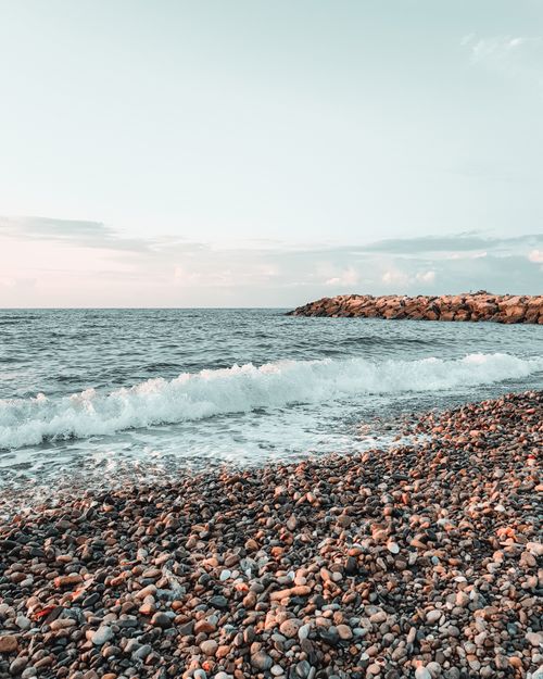 Free Serene seascape featuring a pebble beach, gentle ocean waves, and a tranquil sunrise atmosphere. Stock Photo