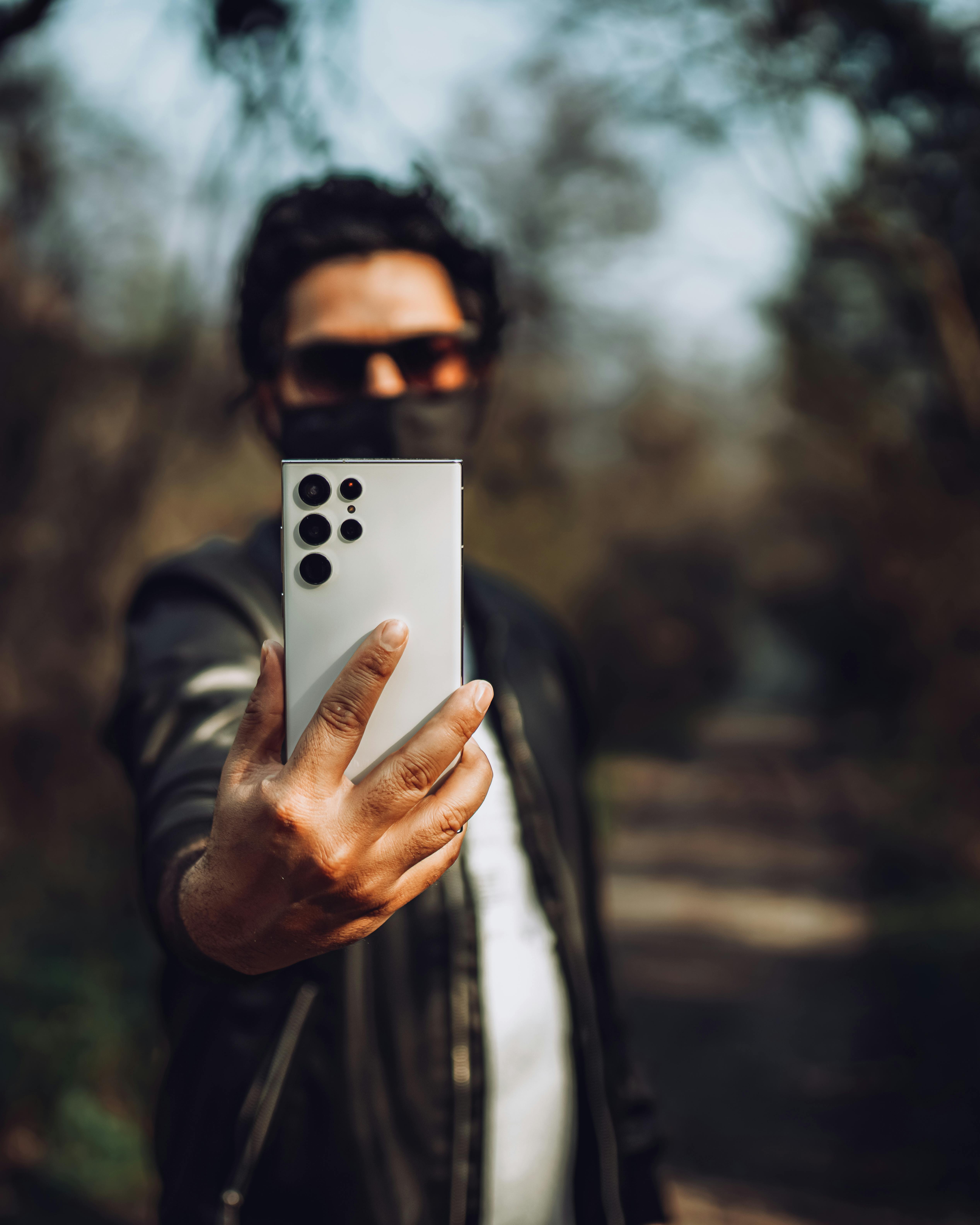 Free Person outdoors holding a smartphone taking a selfie, in a natural setting. Stock Photo