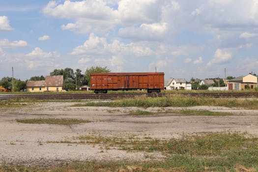 Single freight train car on rural tracks under a cloudy sky in Poland.