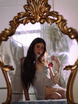 A woman in delicate lingerie holding a pink rose with mirror reflection.