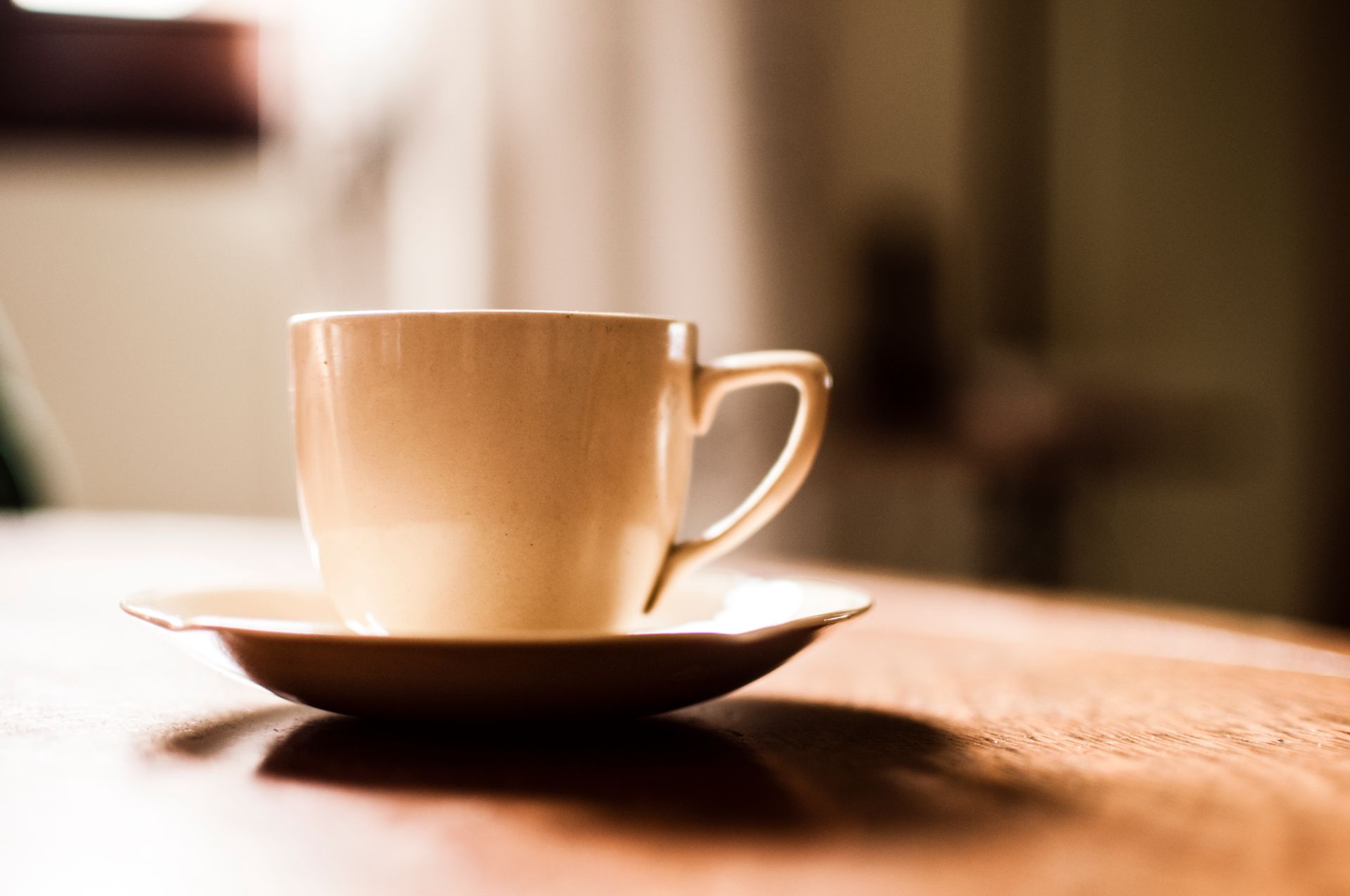 A close-up of a warm porcelain coffee cup on a wooden table in soft lighting.