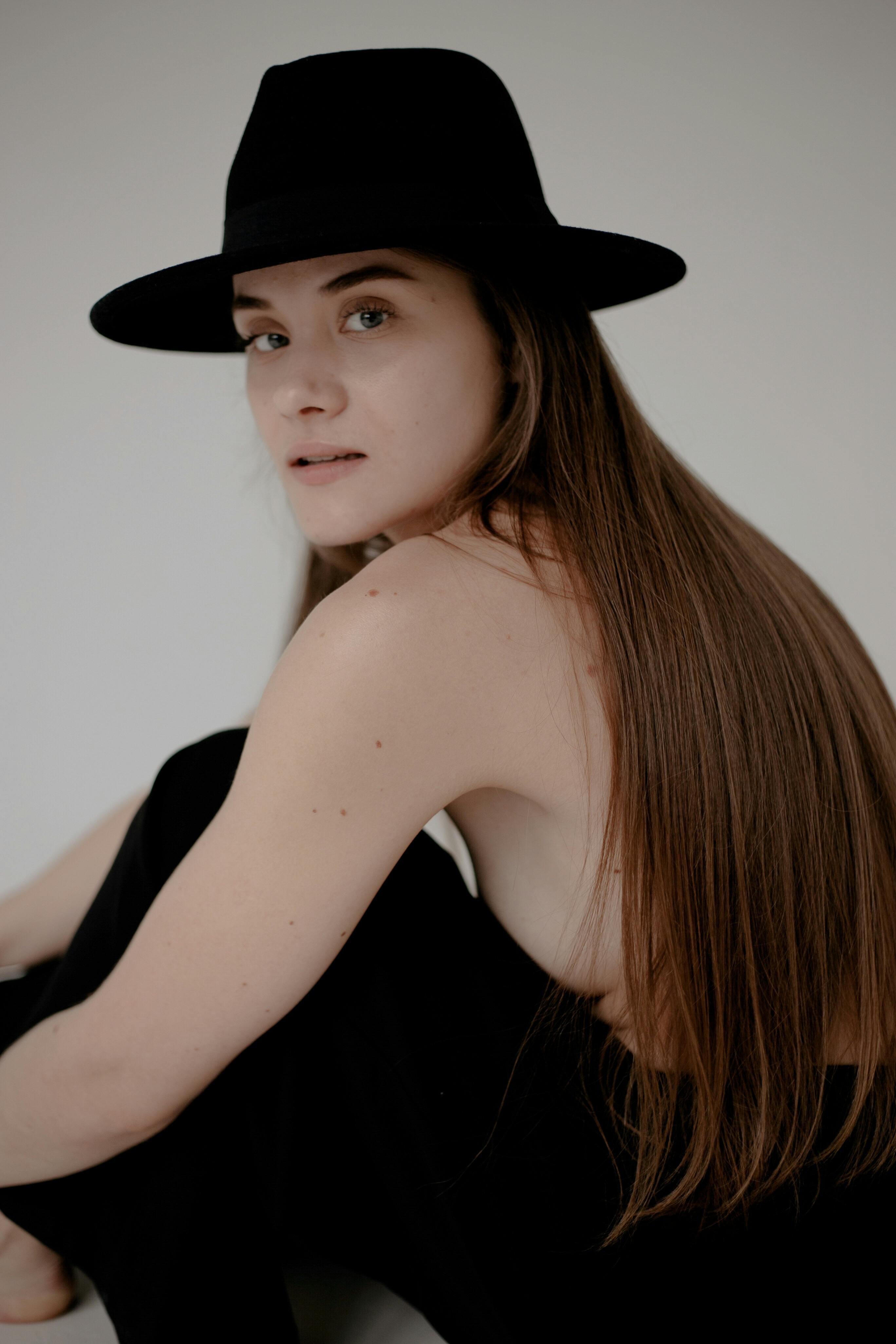 A minimalist studio portrait of a woman wearing a stylish black hat, emphasizing simplicity and elegance.