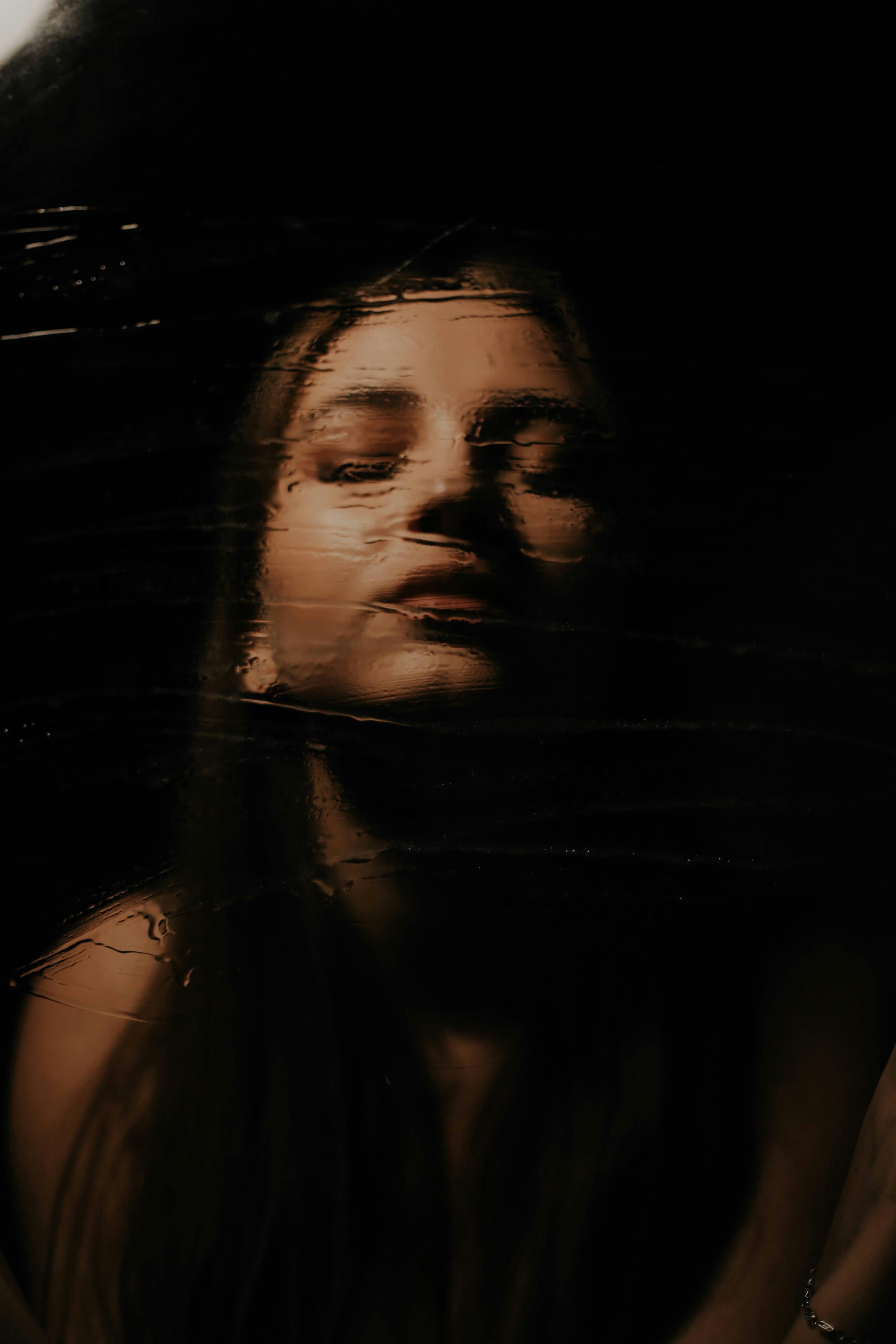 Artistic portrait capturing a woman with eyes closed and a contemplative expression against a dark background.