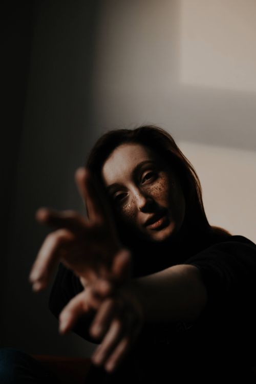 Free Artistic portrait of a woman with fingers reaching towards camera, featuring dramatic shadows and lighting. Stock Photo