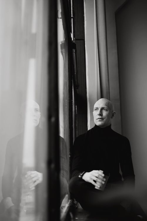 Free Black and white portrait of a pensive bald man in a black turtleneck sitting by a window. Stock Photo
