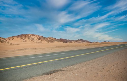Free An empty road stretches through an arid desert landscape under a vibrant blue sky. Stock Photo
