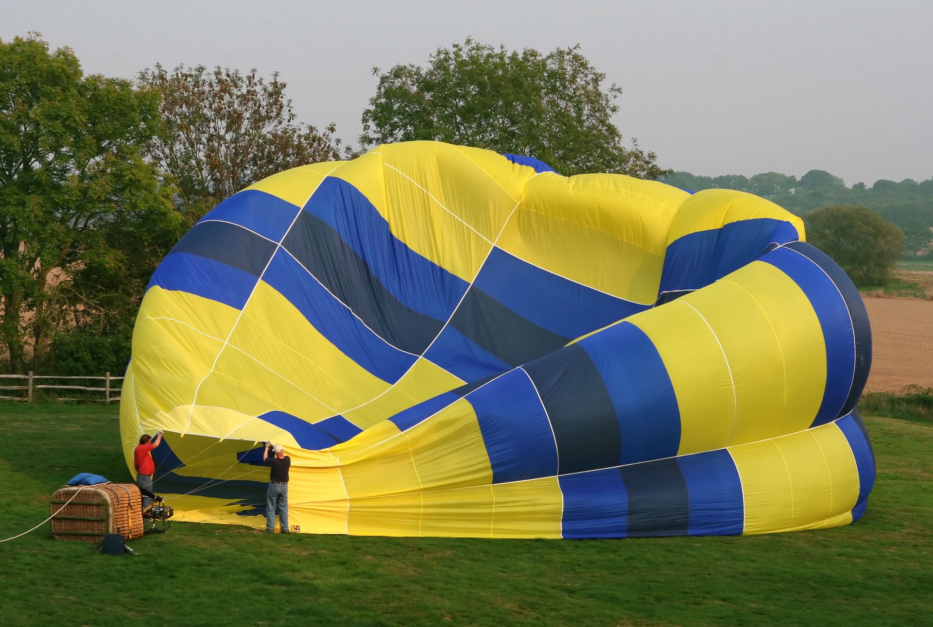 Two men work on inflating a colorful hot air balloon in a green field.
