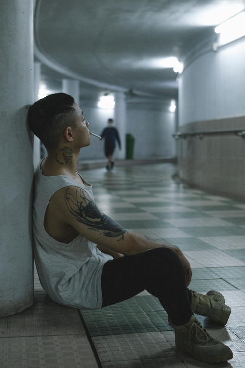 Free Side view of a tattooed man sitting in an urban tunnel, smoking a cigarette. Stock Photo