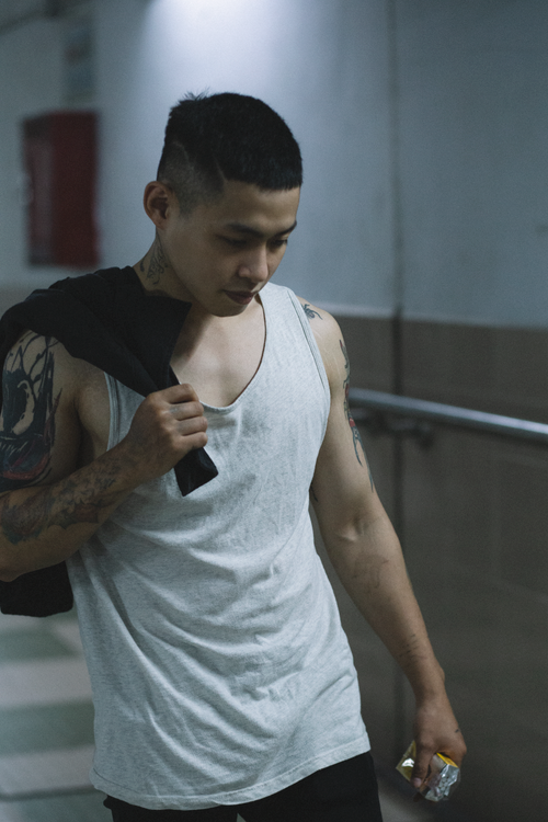 Free A tattooed man in a gray tank top walks indoors, holding a jacket over his shoulder. Stock Photo