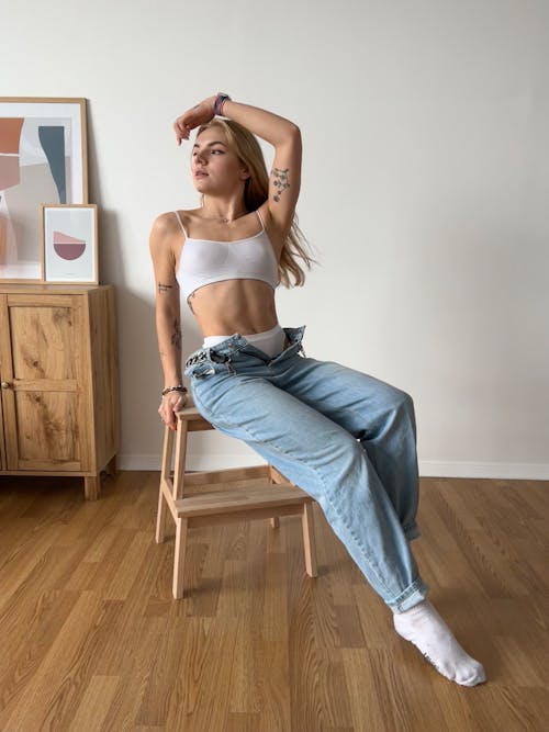 Woman in White Bralette and Denim Jeans Sitting on Wooden Chair 