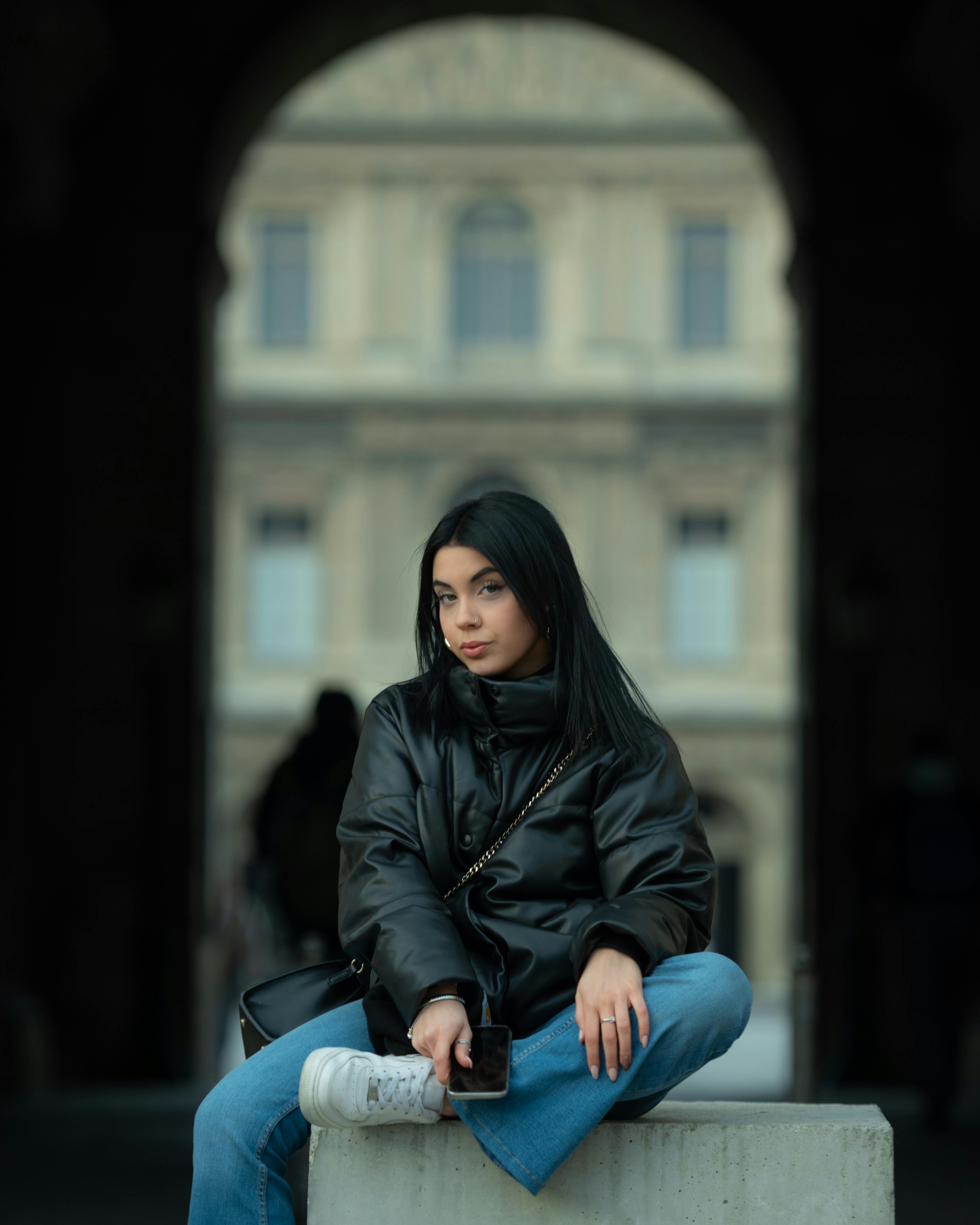 Beautiful young girl wearing black jacket sitting in the street stock photo