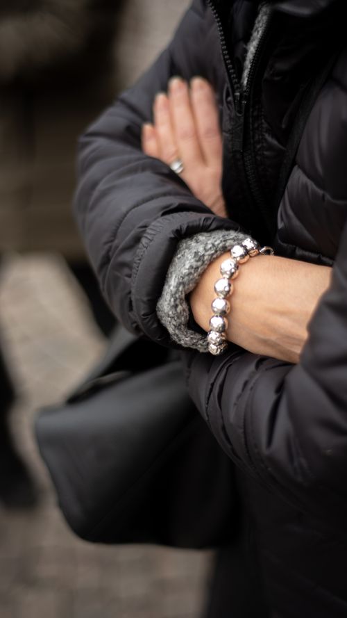 Free Close-up view of crossed arms in a black puffer jacket with a stylish bracelet. Stock Photo