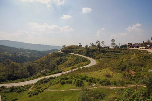 Free A winding mountain road through lush greenery under a clear sky, depicting serene rural beauty. Stock Photo
