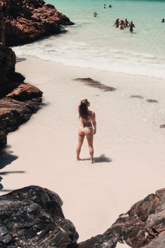 Woman standing on a sunny beach in swimwear, enjoying the ocean view.