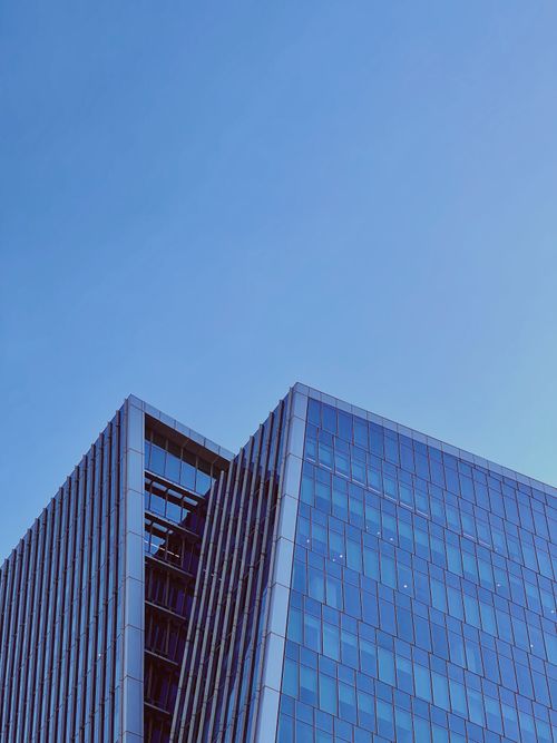 Free Low angle view of a sleek modern skyscraper with a glass facade under a clear blue sky. Stock Photo