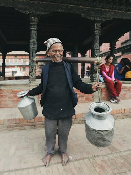 Photo of an Elderly Man Carrying Jugs