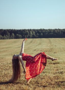 Graceful woman in a red dress dancing in an expansive field under clear skies.