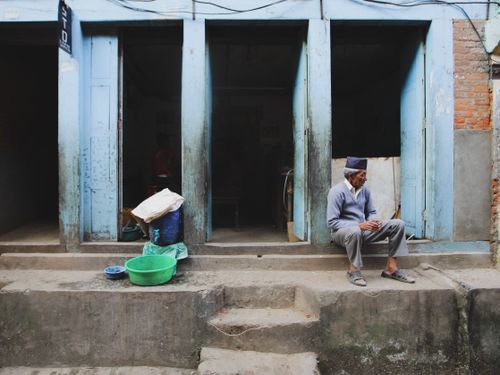 Free Elderly man sits on urban steps, reading a paper, outside a rustic building. Stock Photo