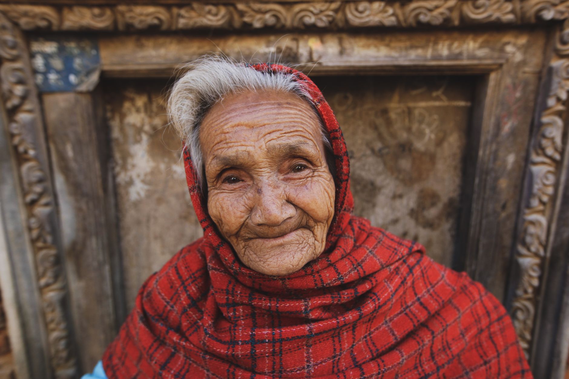 A heartwarming portrait of a smiling elderly woman wearing a red headscarf, showcasing wisdom and kindness.