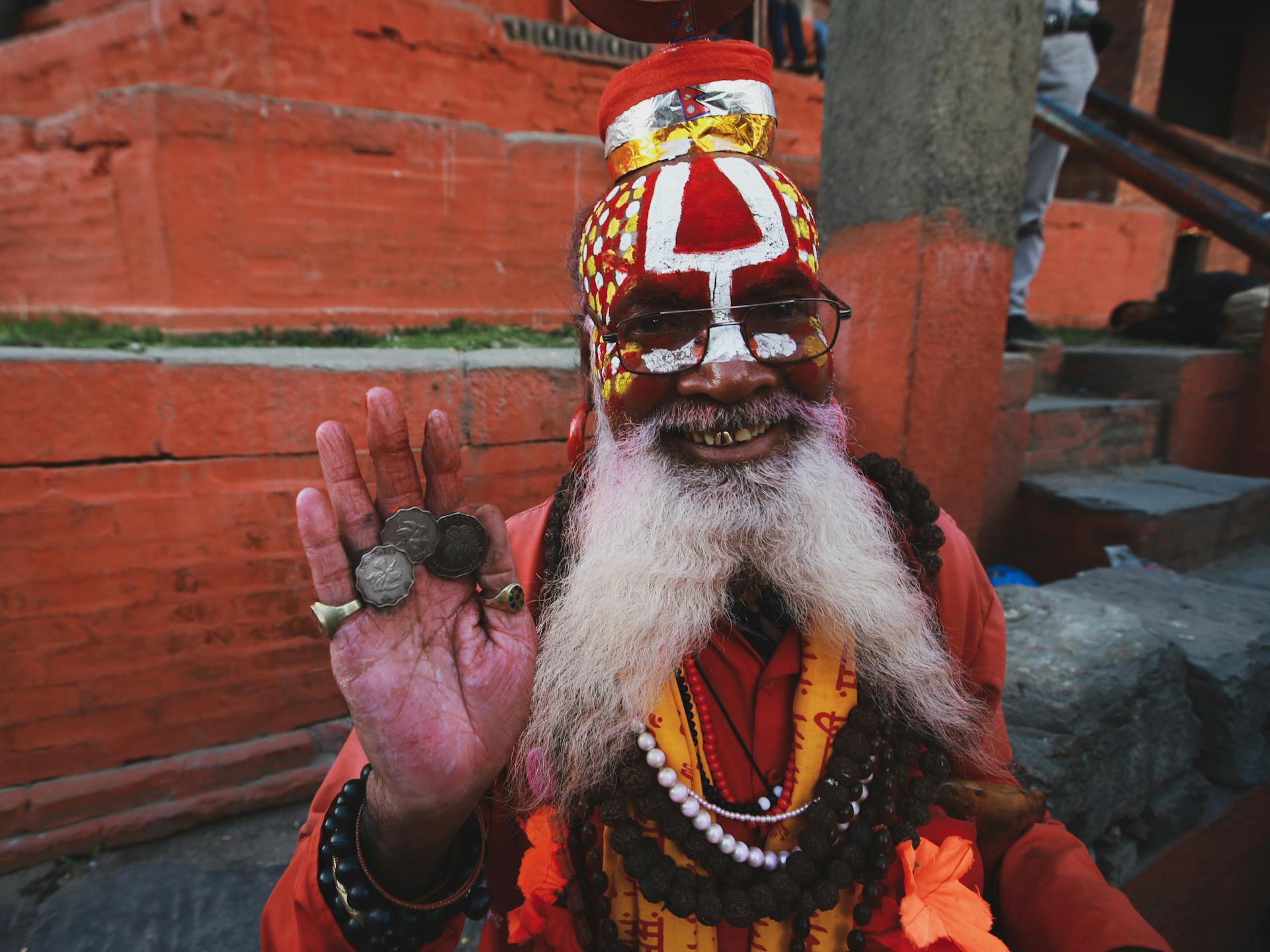 An Elderly Man with Face Paint on His Face with Coins on His Palm Smiling at the Camera