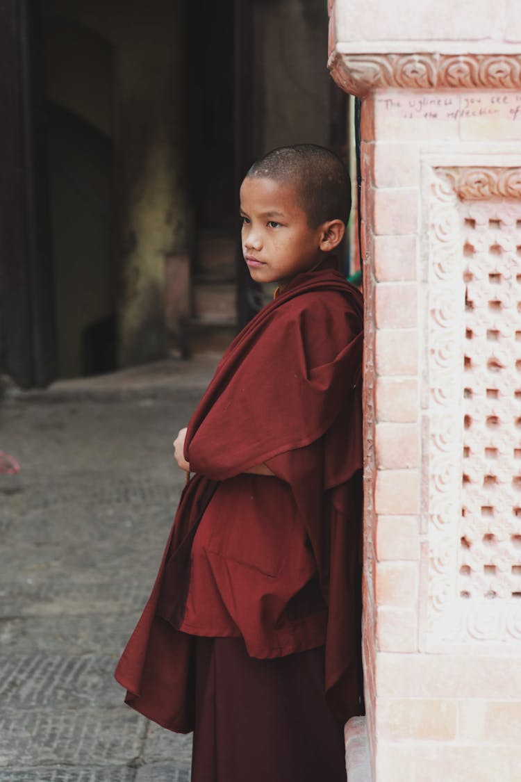 Boy In Red Monk Robes Leaning Against Wall