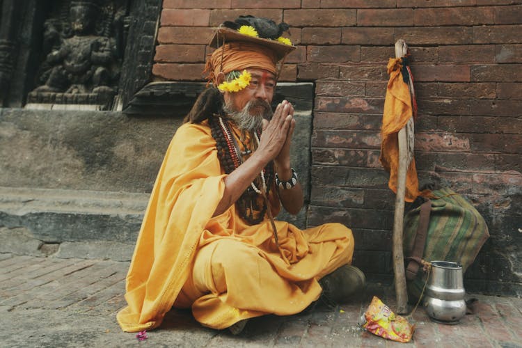 Old Man In Traditional Clothes Sitting On Ground Praying