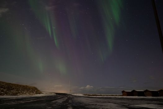 Captivating aurora borealis illuminates a snowy road in Reykjanesbær, Iceland during a clear winter night.