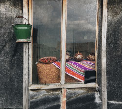 Free A rustic window displaying ceramic pots, a green bucket, and colorful textiles in a rural setting. Stock Photo