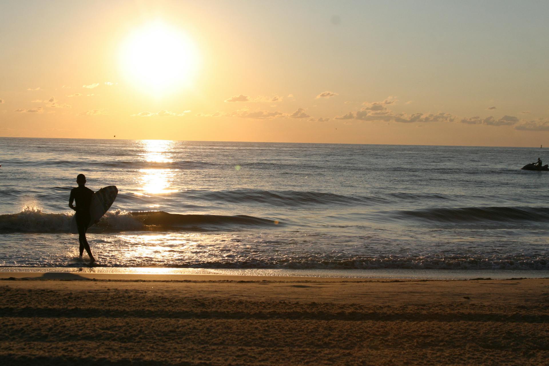 Silhouette of surfer at sunrise on Virginia Beach capturing the tranquil ocean scenery.