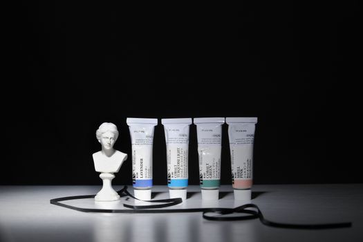 Elegant still life featuring paint tubes and a bust statue against a dark background.