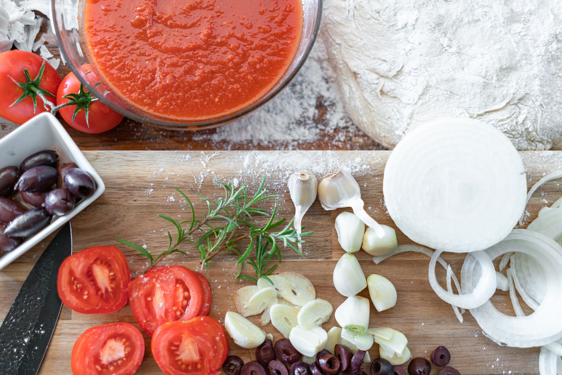 都市生活融入地中海飲食:實用融合策略 A flat lay of fresh tomatoes, garlic, onions, and herbs ready for making a homemade pizza sauce.