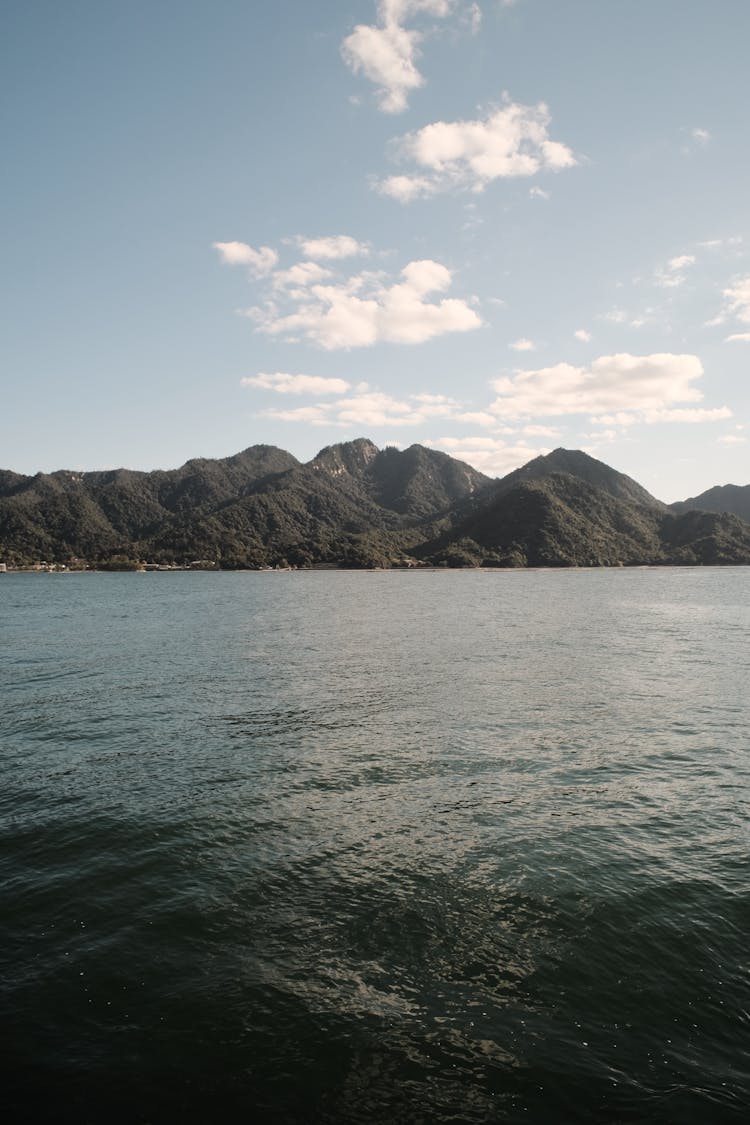 Body Of Water Near Mountain Under Blue Sky And White Clouds