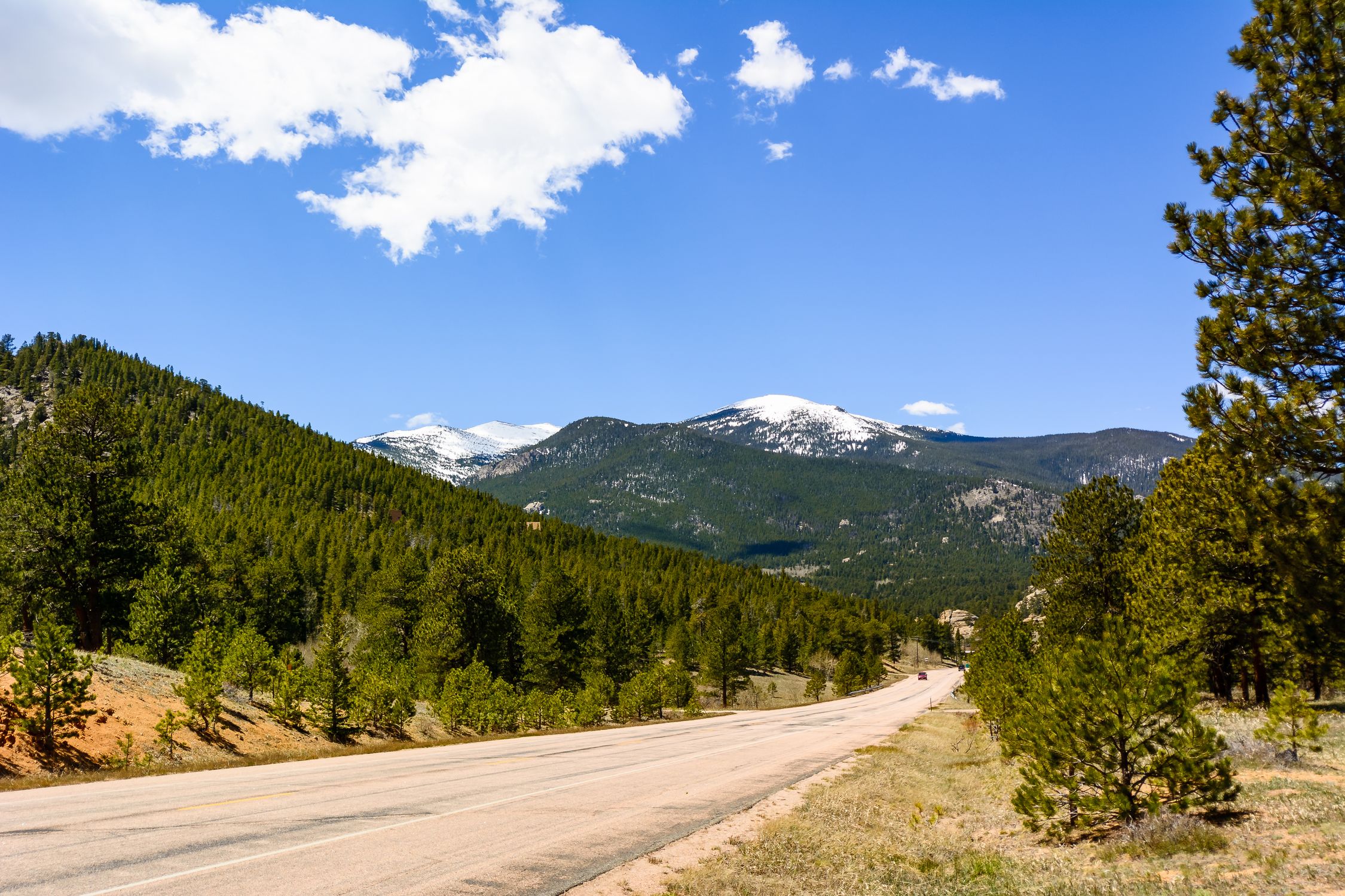 Breathtaking view of snow-capped mountains and coniferous forest from a road in Estes Park, Colorado.